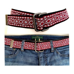 Può includere: Una cintura intrecciata rosso, bianco e nero con una fibbia argentata. La cintura è mostrata su un paio di jeans blu con l'etichetta del marchio "LAUREN JEANS CO. RALPH LAUREN" visibile.
