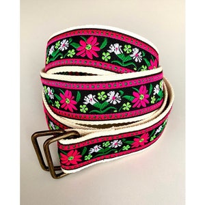 Può includere: Una cintura intrecciata in bianco e nero con ricami floreali rosa e verdi. La cintura è in cotone e ha una fibbia in metallo.