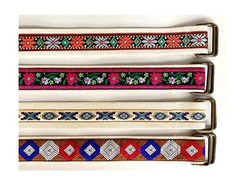 May include: Four different patterned fabric belts with metal buckles. The belts are all white with different colored patterns. The patterns include flowers, geometric shapes, and stripes.