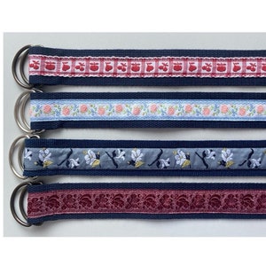 Può includere: Quattro cinture in tessuto diverse con una base blu navy e vari motivi ricamati colorati. Le cinture hanno fibbie ad anello a D argentate.