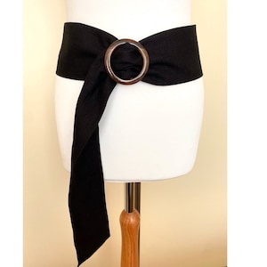 May include: A black fabric belt with a large, round, wooden buckle. The belt is tied in a knot at the front.