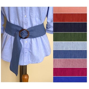 May include: A blue linen belt with a large wooden ring buckle. The belt is shown on a mannequin wearing a light blue shirt. The image also shows a variety of color swatches for the belt.