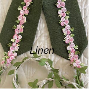 May include: Two green linen fabric ties with pink floral embroidery. The word "Linen" is printed on the fabric.