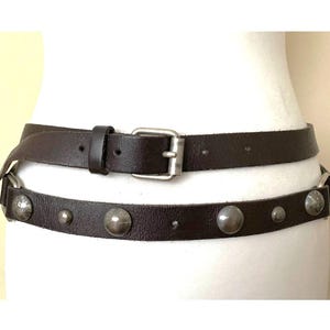 May include: A brown leather belt with silver studs and a silver buckle. The belt is double layered and can be worn as a wrap belt.
