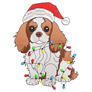 Puede incluir: Un bordado de un Cavalier King Charles Spaniel con un gorro de Papá Noel rojo y envuelto en una guirnalda de luces navideñas de colores. El perro tiene pelo marrón y blanco, ideal para decoraciones navideñas.