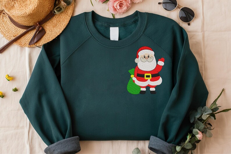 Puede incluir: Una sudadera verde oscuro con un dise&ntilde;o de Pap&aacute; Noel. Pap&aacute; Noel lleva un traje rojo, un cintur&oacute;n negro con hebilla dorada y barba blanca. Sostiene un saco verde. La sudadera tiene cuello redondo y mangas largas.