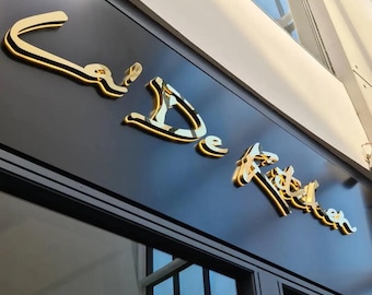 May include: A gold-colored sign with the text "L'De Tache" on a black background.