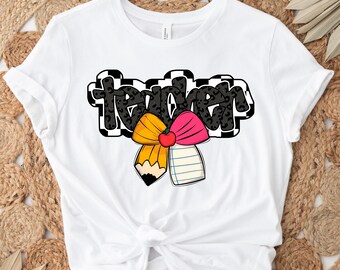 May include: White t-shirt with a black and white chequered design that says "teacher" with a pink and yellow bow with a pencil and notepad in the centre.