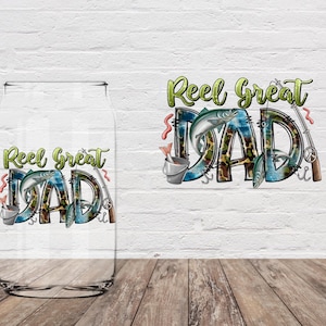 May include: A clear glass can-shaped tumbler with the words "Reel Great Dad" in green and blue, featuring fishing-themed graphics. The design includes a fish, fishing rod, and a bucket with fish. The tumbler sits on a wooden surface.