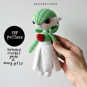 Könnte beinhalten: Eine gehäkelte grüne und weiße Amigurumi-Puppe mit roten Akzenten. Die Puppe hält ein rotes Herz in der Hand. Die Puppe ist ein Charakter aus dem Pokemon-Franchise. Der Text "PDF pattern" befindet sich in einem schwarzen Kreis auf der linken Seite des Bildes. Der Text "Included crochet guide & many gifts!" befindet sich unter dem Kreis.