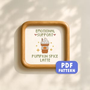 May include: A framed cross-stitch design with the words "EMOTIONAL SUPPORT" and "PUMPKIN SPICE LATTE" above an image of a latte. The frame is a light brown color, and the design includes a PDF pattern label.