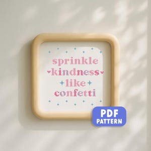 Könnte beinhalten: Ein gerahmtes Kreuzstichmuster mit den Worten "sprinkle kindness like confetti" in Rosa und Blau. Der Rahmen ist aus hellem Holz und der Hintergrund ist weiß. Ein blauer und violetter PDF-Muster-Button befindet sich in der unteren rechten Ecke.
