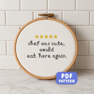 May include: A cross-stitch embroidery hoop with the text "chef was cute, would eat here again." The design includes five gold stars above the text. The hoop is made of wood and has a PDF pattern button.