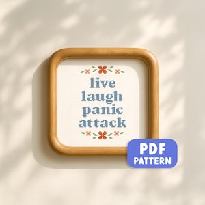 Puede incluir: Un diseño de punto de cruz enmarcado con las palabras "live laugh panic attack" en azul, rodeado de detalles florales. El marco de madera tiene esquinas redondeadas. Un botón azul "PDF PATTERN" está en la esquina inferior derecha.