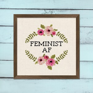 May include: A cross-stitch embroidery with a floral wreath design and the text "Feminist AF".