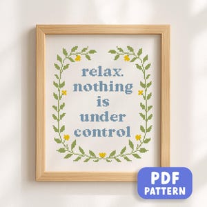 May include: A framed cross-stitch artwork with the words "relax. nothing is under control" in blue, surrounded by a green and yellow floral border. The frame is light brown. A blue PDF pattern button is in the bottom right corner.