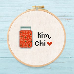 May include: A white embroidery hoop with a red and green illustration of a jar of kimchi and the text "kimchi" with a red heart.