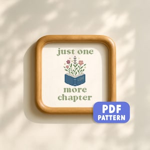 May include: A framed cross-stitch design with the text "just one more chapter." The design features an open blue book with flowers and the word "LOVE." The frame is a light brown colour, and a blue PDF pattern button is in the lower right corner.