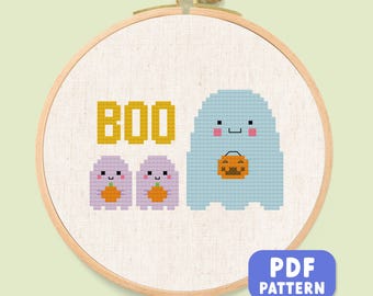 May include: A cross-stitch design in a wooden hoop. The design shows the word "BOO" in yellow, two small purple ghosts with pumpkins, and a larger blue ghost holding a pumpkin. A blue rectangle with "PDF PATTERN" is in the bottom right.