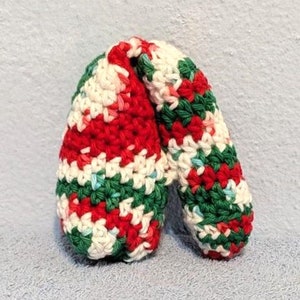 May include: A handmade crochet item in a Christmas color scheme. The item is primarily red, white, and green, with a striped pattern. The item appears to be a decorative piece or a small toy.