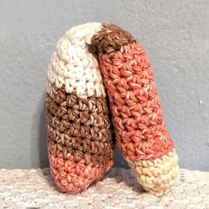 May include: A crocheted toy shaped like a candy cane with brown, white, and pink stripes.
