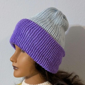 May include: A two-tone knit beanie in a light blue and purple color scheme. The hat features a ribbed knit design, with the purple section forming the brim. The beanie is displayed on a mannequin head.