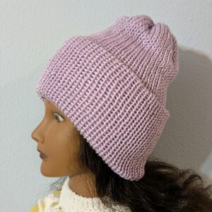 May include: A light purple knit beanie hat. The hat is made of a ribbed knit fabric and has a folded brim. The hat is shown on a mannequin head. The hat is a winter accessory.