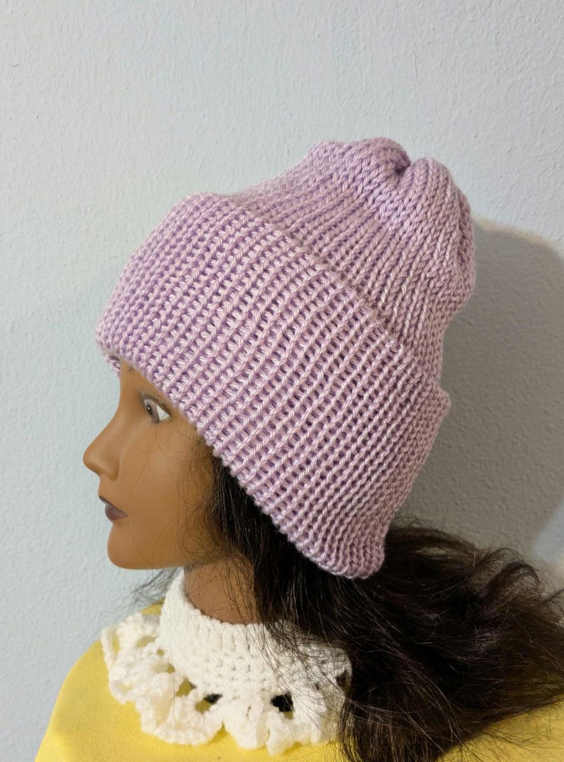 May include: A light purple knit beanie hat. The hat is made of a ribbed knit fabric and has a folded brim. The hat is shown on a mannequin head. The hat is a winter accessory.