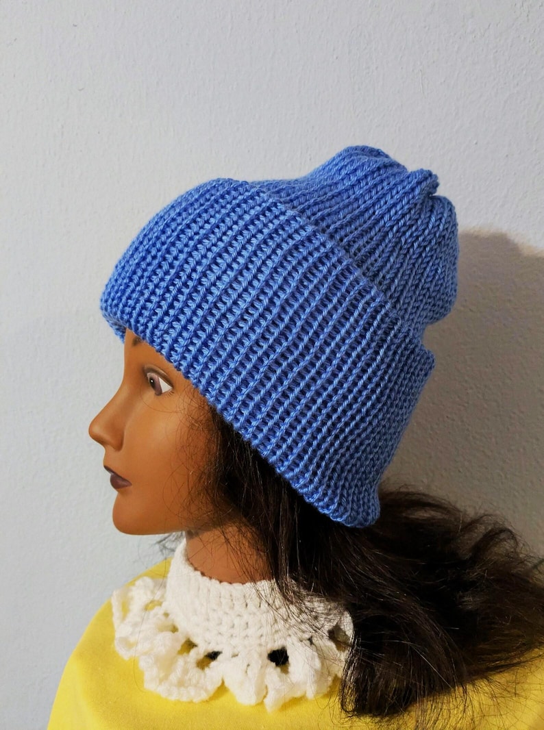 May include: A blue knitted beanie hat. The hat is made of a ribbed knit fabric and has a folded brim. The hat is a solid light blue color. The hat is shown on a mannequin head.