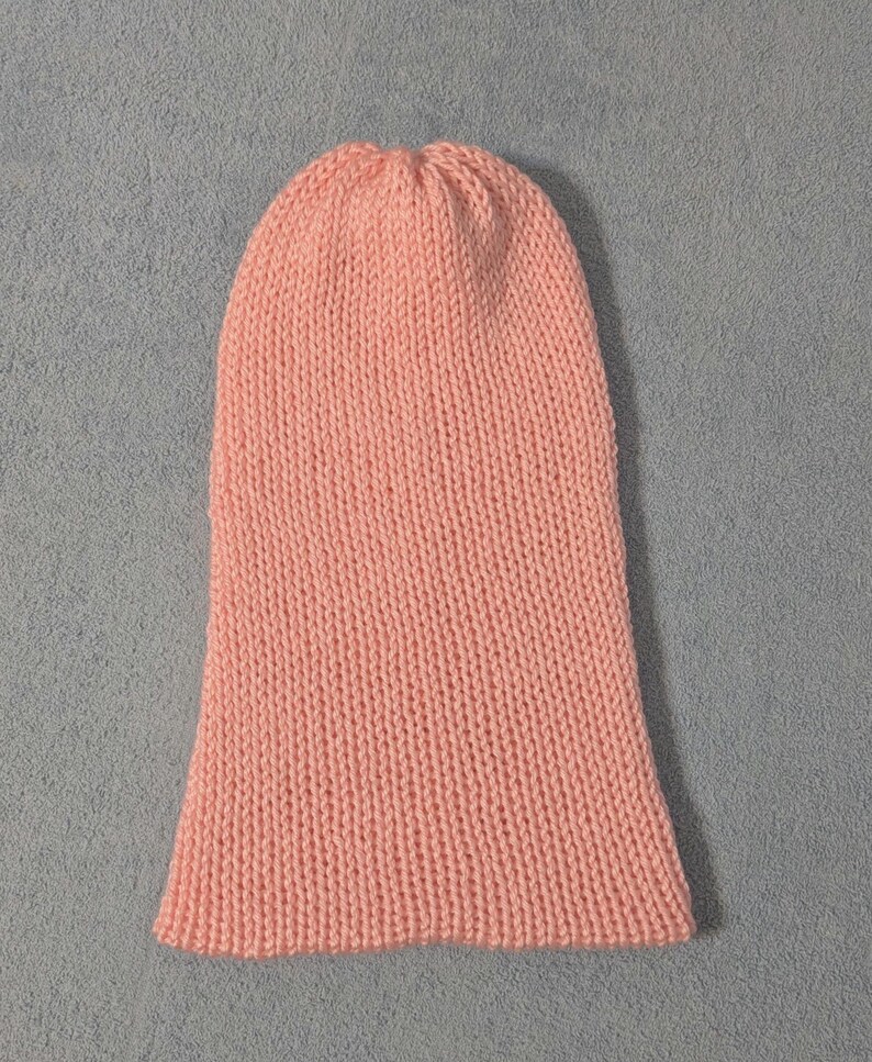 May include: A light peach-colored knitted beanie hat. The hat is made of a soft, textured yarn and has a close-fitting design. The hat is a solid color and is suitable for cold weather.