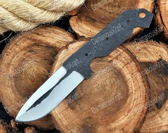May include: A knife blade with a silver edge and a dark, textured handle. The blade is lying on a wooden surface. The text "DamascusKraft" is visible on the blade and the wooden surface.