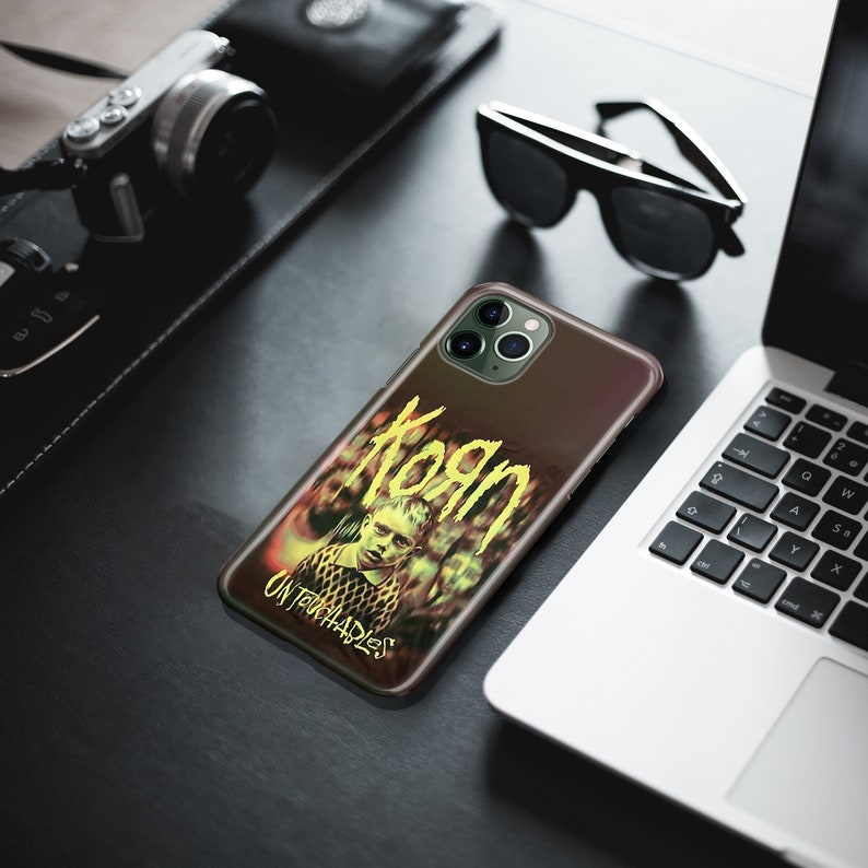 May include: A black iPhone case with a graphic of the band Korn and the album title "Untouchables". The case has a yellow and green color scheme.