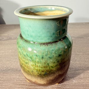 May include: A ceramic vase featuring a gradient glaze that transitions from a light turquoise at the rim to a deep forest green and earthy brown at the base. The surface displays a fine crackle pattern throughout the glossy finish.