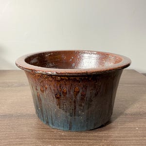 May include: A handcrafted ceramic bowl with a wide, rounded rim. The exterior features a blend of brown and blue hues, creating a unique, textured appearance. The bowl is suitable for decorative or functional use.