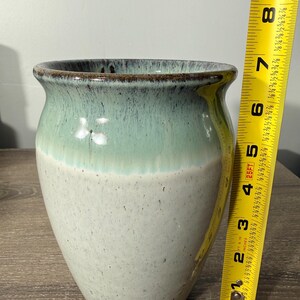 May include: A handcrafted ceramic vase with a two-tone glaze. The top portion is a seafoam green, transitioning to a speckled off-white base. The vase is approximately 7 inches tall and has a wide opening.