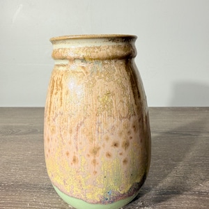May include: A ceramic vase with a rounded body and a flared rim. The glaze features a gradient of colors, transitioning from a light mint green at the base to a mottled blend of yellow, pink, and brown tones with a textured, crystalline finish.
