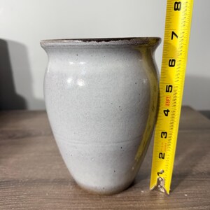 May include: A light blue ceramic vase with a dark brown rim. The vase is approximately 7 inches tall. The vase has a speckled texture and a slightly flared top. The vase is on a wooden surface.