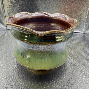 May include: A set of three ceramic mugs with a speckled, cream-colored glaze. Each mug features a different hand-painted design: a blue and green leaf, a yellow flower, and a red berry. The mugs have a simple, rounded shape.