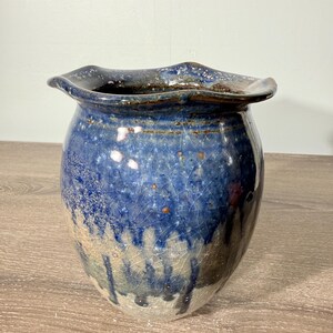 May include: A ceramic vase with a wide, ruffled rim and a bulbous body. The glaze features a deep blue color at the top that transitions into a lighter, mottled beige and grey base, characterized by a prominent crackle finish and small brown spots.