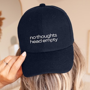 May include: A navy blue baseball cap featuring the embroidered white text "no thoughts head empty" centred on the front panel. The cap has a structured crown, a curved brim, and a button at the top, showcasing a clean and simple design.
