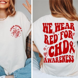 May include: White t-shirt with red text and graphic. The front of the shirt says "Team Custom" with a red heart and flowers. The back of the shirt says "We Wear Red For CHD Awareness" with a red heart and ribbon.