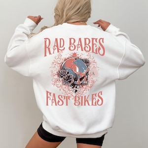 May include: White sweatshirt with a pink graphic of a skull with roses and the text "Rad Babes Fast Bikes".
