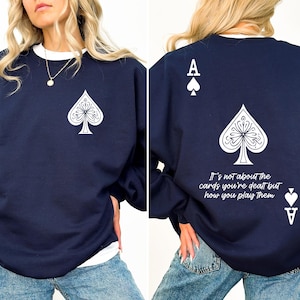 May include: A navy blue sweatshirt with a white ace of spades graphic on the front and back. The back graphic also includes the text "It's not about the cards you're dealt but how you play them."