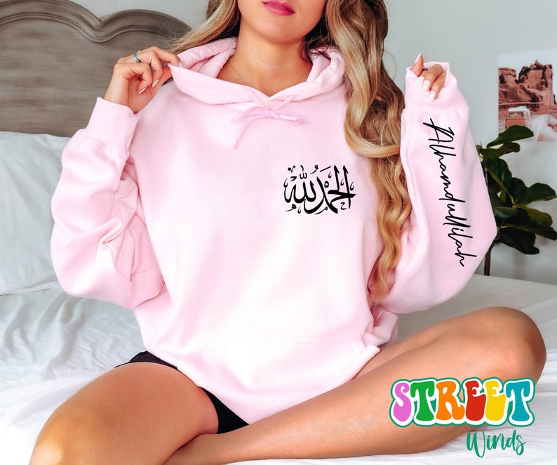 May include: Pink hoodie with a black Arabic calligraphy design on the front and the text "Alhamdulillah" on the sleeve.