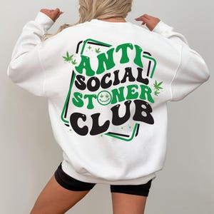 May include: White sweatshirt with a green and black graphic print that says "Anti Social Stoner Club" with a smiley face and marijuana leaf designs.
