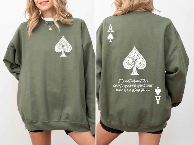 May include: A green sweatshirt with a white ace of spades design on the front and back. The back design includes the text "It's not about the cards you're dealt but how you play them."