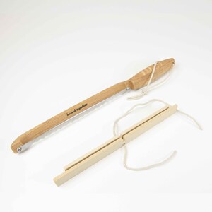 May include: A wooden saw with a serrated blade and a wooden handle. The saw is tied to a wooden frame with a string. The saw is labeled "handmade in sweden".