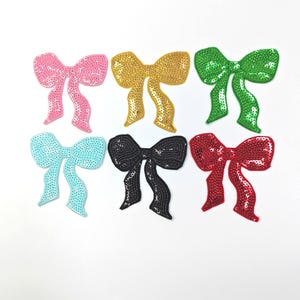 Puede incluir: Seis apliques de lazo con lentejuelas en varios colores: rosa, dorado, verde, azul claro, negro y rojo. Cada lazo tiene una forma clásica con una superficie texturizada y brillante. Ideales para adornar ropa o accesorios.