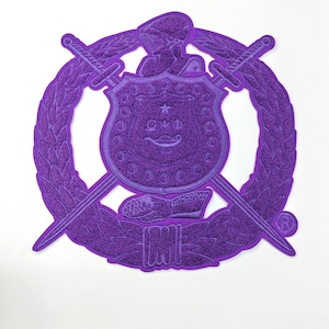 Peut inclure: Un écusson brodé violet représentant un bouclier, des épées croisées et une couronne de laurier. L'écusson comprend un casque de chevalier et le texte "ΩΨΦ". L'écusson mesure 26 cm sur 26,2 cm.