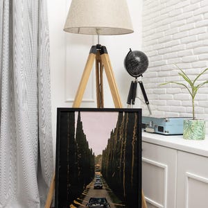 May include: A black and white framed print of a vintage photograph of a line of black cars driving down a road lined with tall trees.